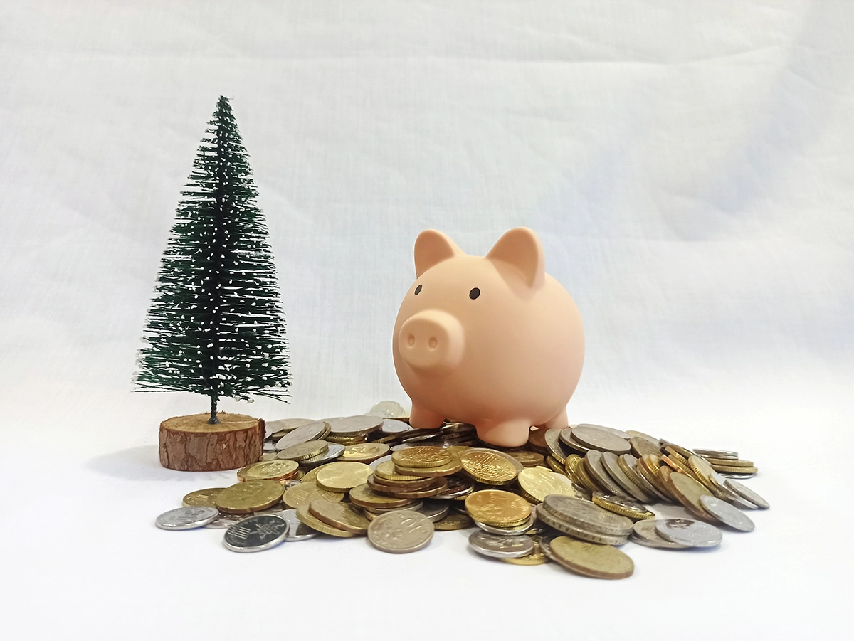 Piggy bank atop a pile of coins next to a toy pine tree